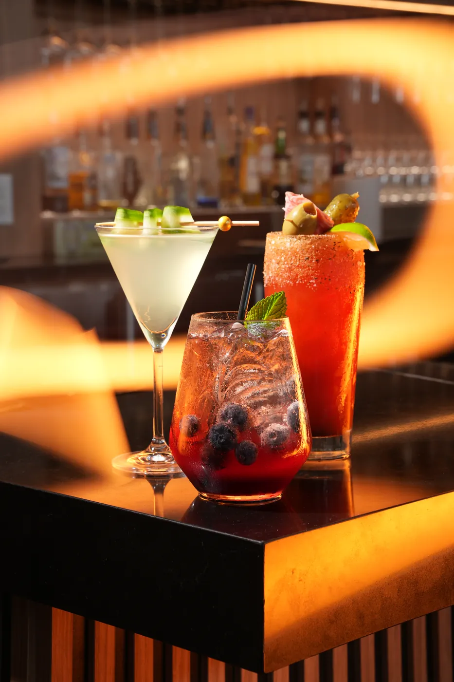 Three cocktails on a bar counter, framed by a warm orange light
