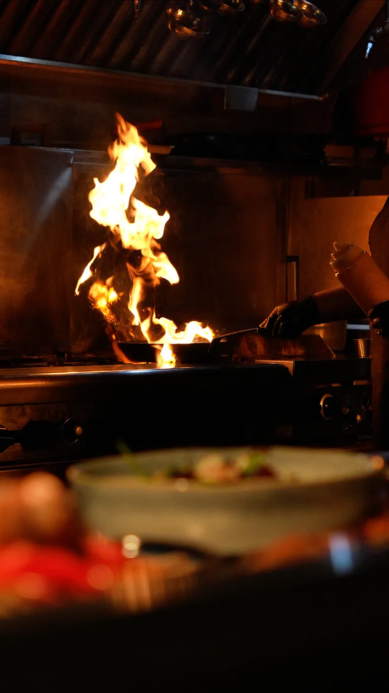 Chef flambéing a pan, flames rising in a dark kitchen