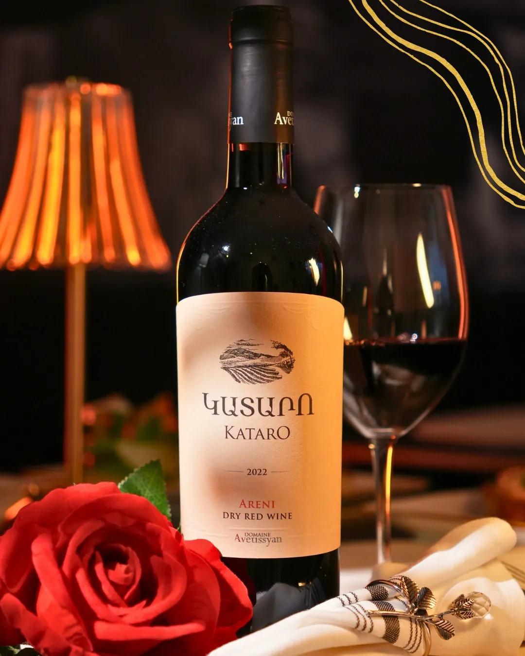 Bottle of Armenian red wine beside a glass, a rose and a warm table lamp